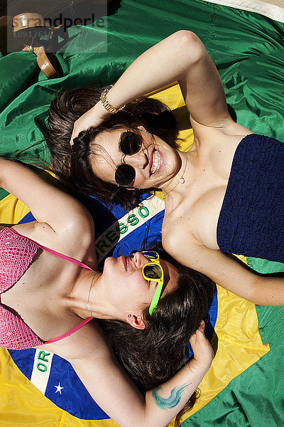 Zwei Freunde in Strandkleidung  liegend auf brasilianischer Flagge