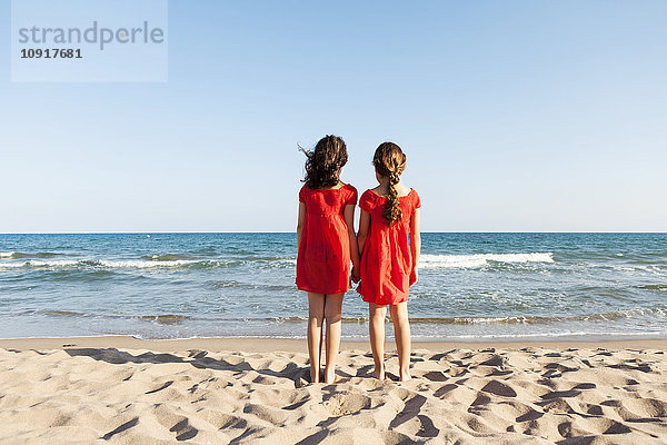 Rückansicht von zwei kleinen Schwestern am Strand mit Blick auf das Meer