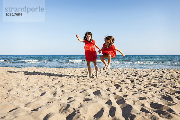 Zwei kleine Schwestern springen zusammen am Strand.