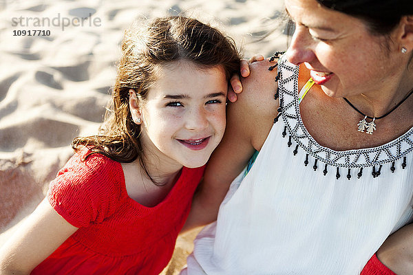 Porträt eines glücklichen kleinen Mädchens neben ihrer Mutter am Strand