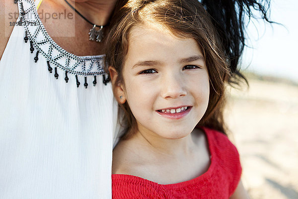 Porträt eines lächelnden kleinen Mädchens neben ihrer Mutter am Strand