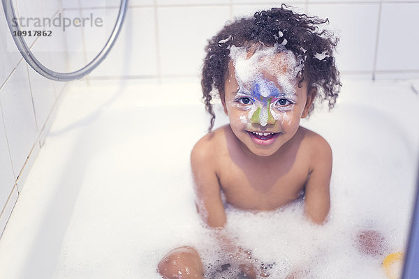Porträt eines lächelnden kleinen Mädchens mit gemaltem Gesicht in einer Badewanne sitzend