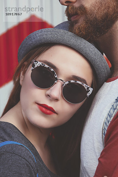 Portrait einer jungen Frau mit Sonnenbrille  die sich gegen ihren Freund lehnt.