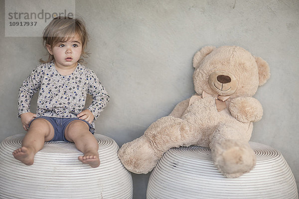 Seriöses Mädchen und Teddybär auf Hockern sitzend