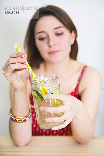 Frau hält ein Glas Entgiftungswasser mit Zitrone und Gurke in der Hand