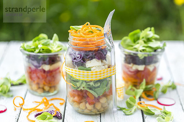 Regenbogensalat im Glas mit Kichererbsen  Tomaten  Karotten  Rotkohl  Radieschen  Salat und Fetakäse