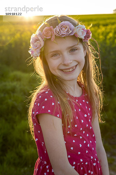Porträt eines lächelnden Mädchens mit Blumenkranz auf einem Rapsfeld