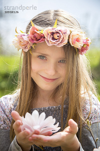 Porträt eines lächelnden Mädchens mit Blumenkranz mit Magnolienblüte in den Händen