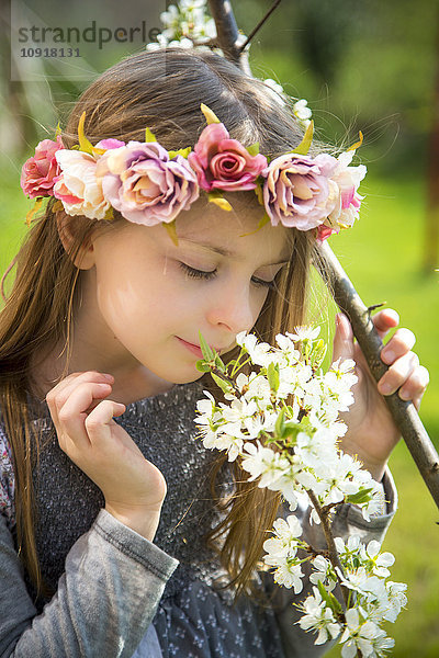 Kleines Mädchen mit Blumenkranz duftend blühendem Ast