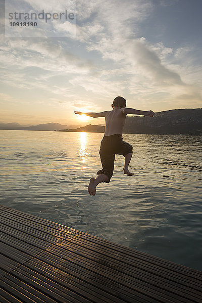 Italien  Veneto  Bardolino  Gardasee  Junge beim Sonnenuntergang ins Wasser springen