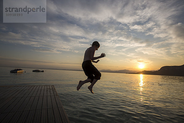Italien  Veneto  Bardolino  Gardasee  Junge beim Sonnenuntergang ins Wasser springen