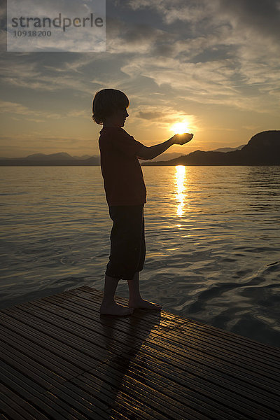 Junge hält bei Sonnenuntergang die Hände gegen die Sonne.