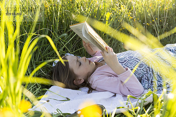 Kleines Mädchen  das auf einem Blumenfeld liegt und ein Buch liest.