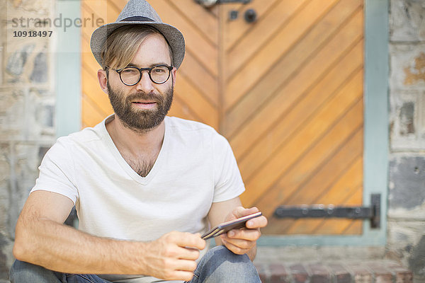Bärtiger Mann im Freien mit Handy mit Hut und Brille