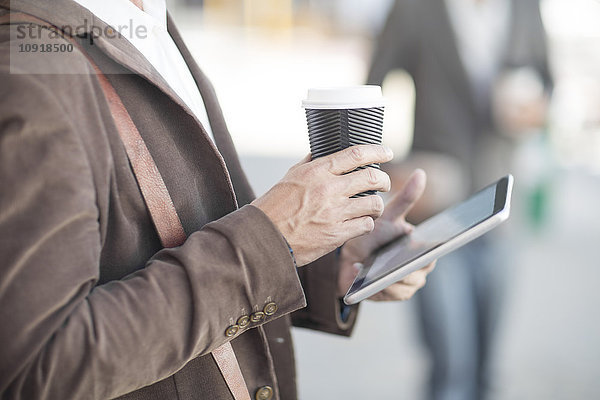 Mann mit digitalem Tablett und Kaffee für unterwegs