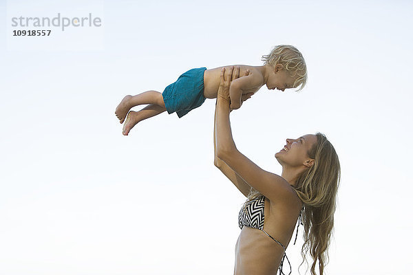 Glückliche Mutter im Bikini hebt ihren Sohn hoch