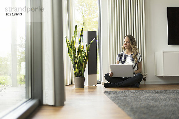 Frau zu Hause sitzend auf dem Boden mit Laptop