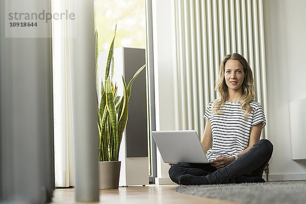 Frau zu Hause sitzend auf dem Boden mit Laptop