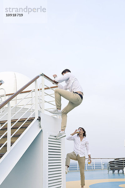 Zwei junge Männer  die sich auf einem Kreuzfahrtschiff herumtreiben und auf ein Geländer klettern.