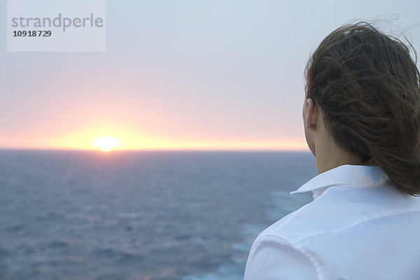 Junger Mann mit Blick auf den Sonnenuntergang über dem Meer