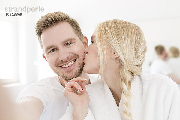 Mann nimmt Selfie von Freundin  die ihn küsst.