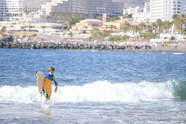 Spanien  Teneriffa  Junge mit Surfbrett im Meer