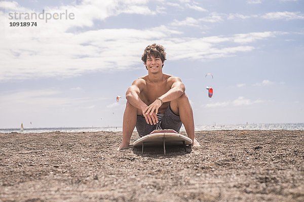 Porträt eines lächelnden jungen Mannes auf dem Surfbrett am Strand