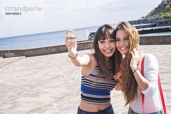 Zwei lächelnde Freunde an der Küste mit einem Selfie
