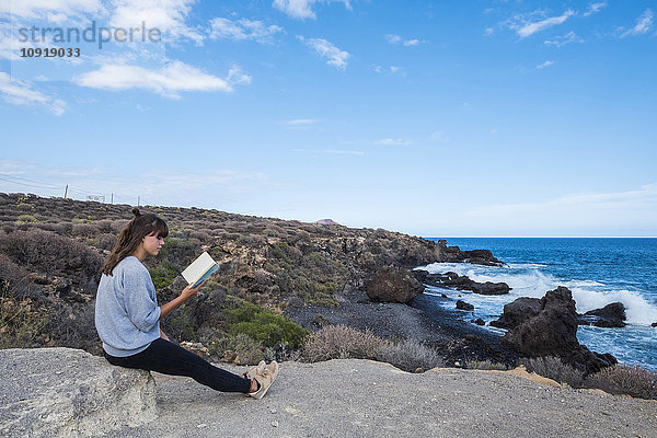 Junge Frau liest Buch am Meer
