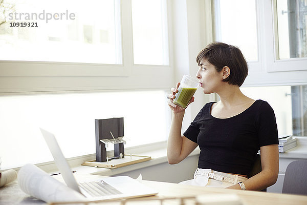 Porträt einer Frau  die im Büro grünen Smoothie trinkt