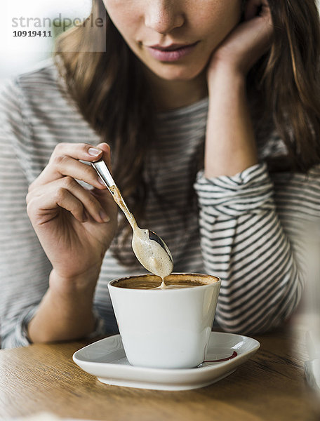 Junge Frau trinkt Cappuccino  Löffelchen Milchschaum