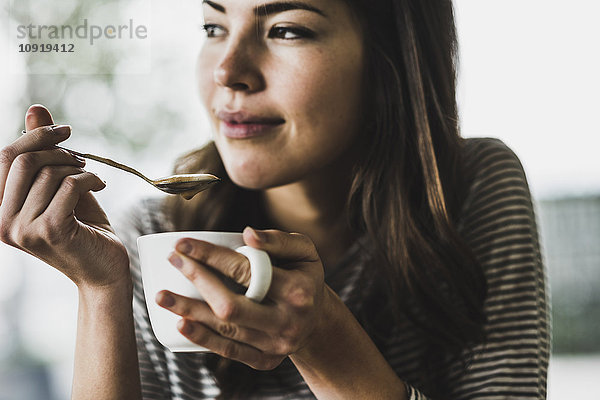 Junge Frau trinkt Cappuccino  Löffelchen Milchschaum