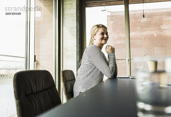 Lächelnde junge Frau am Schreibtisch im Büro
