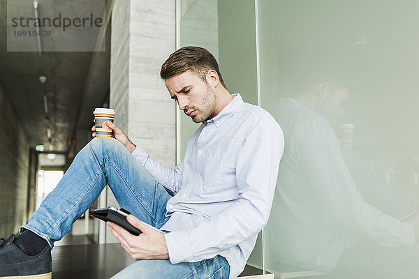 Junger Mann auf dem Boden sitzend mit digitalem Tablett