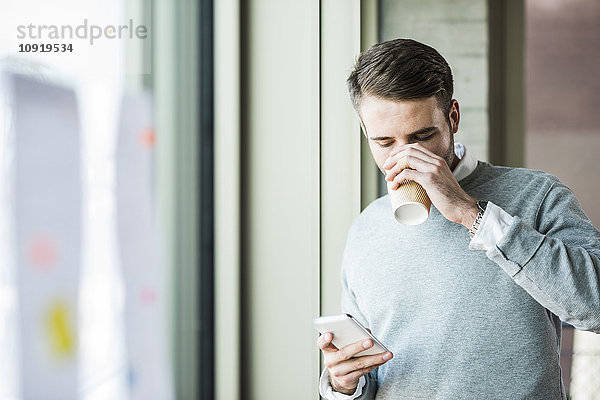 Junger Mann mit Kaffee zum Anschauen des Handys