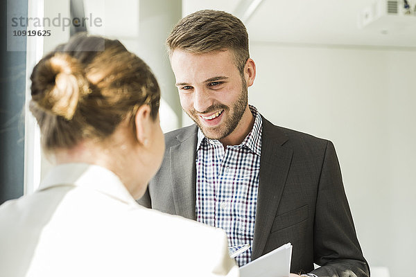 Lächelnder junger Mann mit Blick auf einen Kollegen im Büro