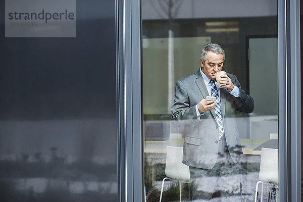 Senior Geschäftsmann mit Kaffee zum Suchen auf dem Handy