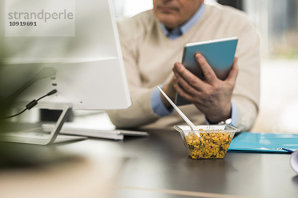 Senior Mann im Büro  hält digitale Tablette  Salat in Plastikschale auf Schreibtisch