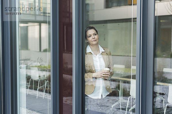 Senior Managerin auf der Fensterscheibe stehend  Kaffeetasse