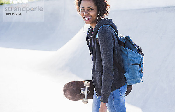 Fröhliche junge Frau mit Skateboard beim Musikhören