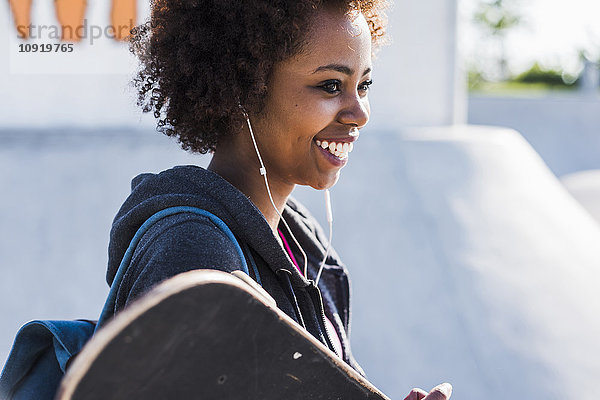 Lächelnde junge Frau mit Skateboard beim Musikhören