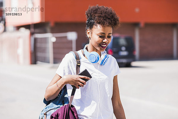Lächelnde junge Frau mit Kopfhörer und Handy im Freien