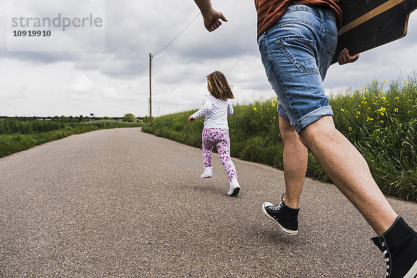 Vater mit Skateboard und Tochter läuft auf dem Landweg