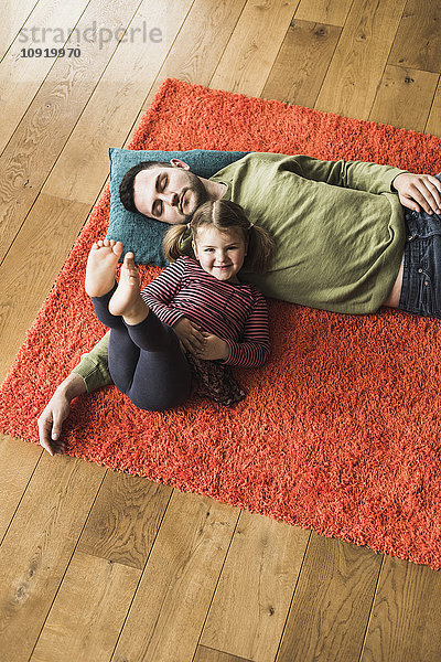 Vater und Tochter liegen auf einem Teppich auf dem Boden.