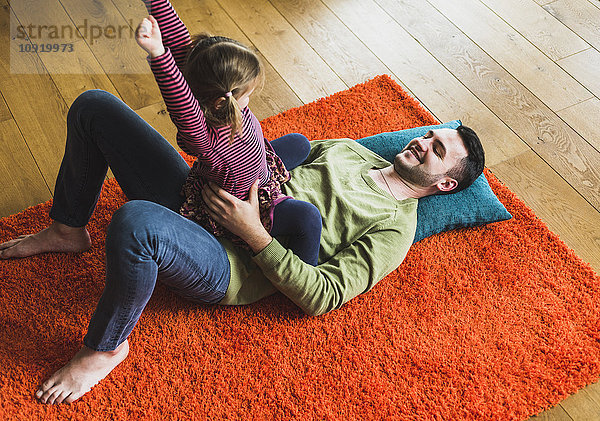 Verspielter Vater und Tochter liegen auf einem Teppich auf dem Boden.