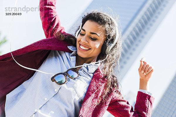 Fröhliche junge Frau mit Kopfhörern  die sich im Freien bewegen.