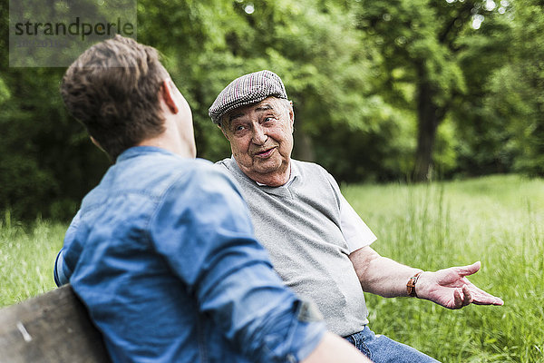 Porträt eines älteren Mannes  der auf einer Bank sitzt und mit seinem Enkel spricht.