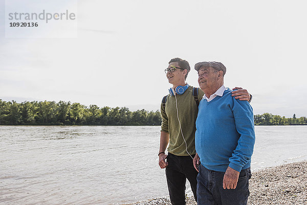 Großvater und Enkel stehen am Flussufer und schauen gemeinsam in die Ferne.