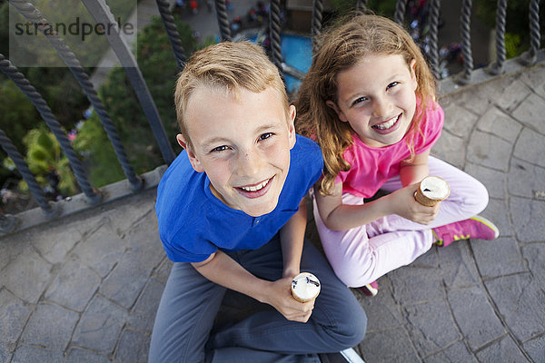 Porträt von Bruder und Schwester mit Eistüten auf dem Balkon mit Blick zur Kamera
