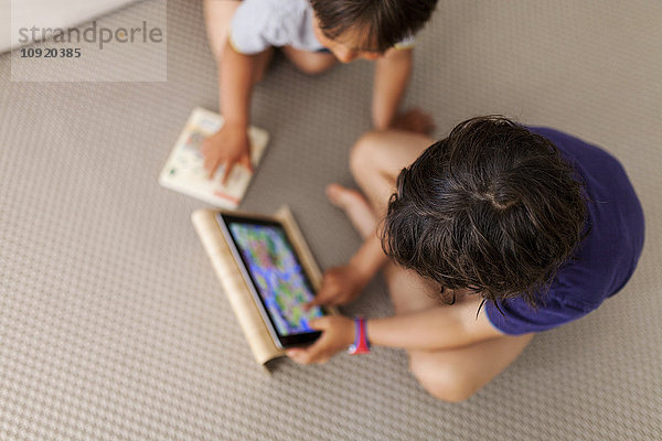Kleiner Junge sitzt auf dem Boden und benutzt ein digitales Tablett  während sein Bruder zuschaut.